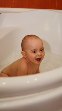 Funny little child smiling and playing with water in a bathroom. Toddlers bathes.の写真素材