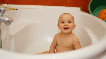 Funny smiling little child smiling and playing with water in a bathroom. Toddlers bathes.の写真素材