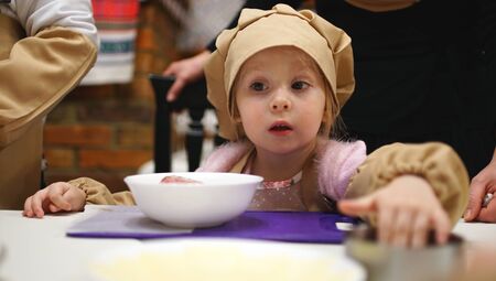 Little girl in a cooking caps and aprons with interested look playing in cafe. Concept of cooking classesの写真素材