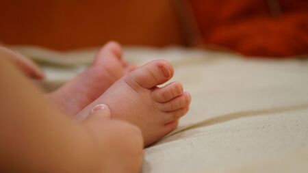 Little baby boy foot in hands of his mother in bed. Family morning at home.の写真素材