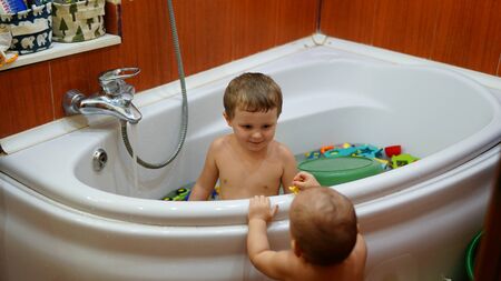 Funny little two brothers playing in tub of the bathroom.