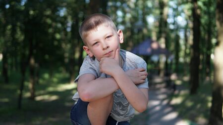 Close up portrait of caucasian teen boy. Funny cute teenager in summer park at day. Child holding his chin looking at camera.の写真素材