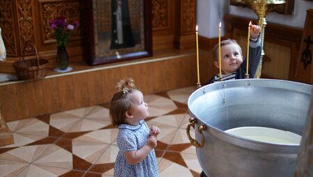 Little boy and girl near the font in Orthodox Church, first visit and first impression in a Church. Boy lights a candleの写真素材