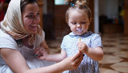 Little girl holding the candle with her mom in Orthodox Church, first visit and first impression in a Churchの写真素材