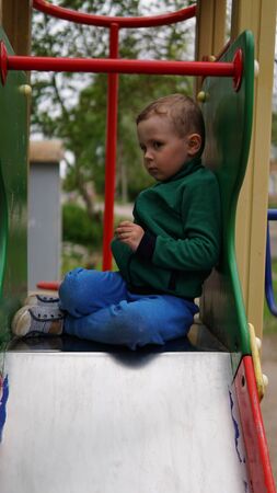 Smiling little boy sitting on a top of slide and funny seriousの写真素材