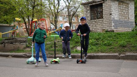 Three smiling adorable little children riding on kick scooters at playground. Children jump together.の写真素材