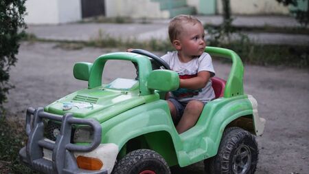 Little preschool boy driving big toy green car and having fun, outdoors. Active leisure with kids on warm summer day.の写真素材