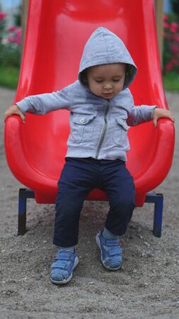 Little boy having fun on a playground outdoors in summer. Toddler on a red slide.の写真素材