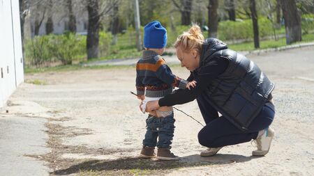 Mother straighten baby's clothes outdoors near garageの写真素材