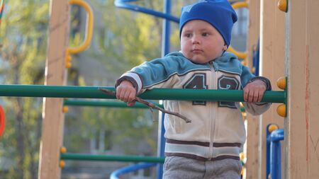 Cute little boy portrait in a blue hat climbs stairs on the playground in cityの写真素材