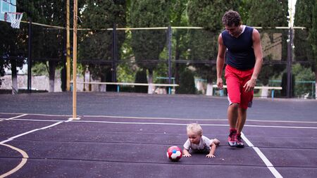 Athletic father and his little son playing on basketball playground. Father and son spending together free time in spring day.の写真素材