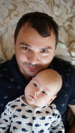 Portrait of loving young man with baby at home . Close up of happy smiling black haired father holding his cute toddler .の写真素材