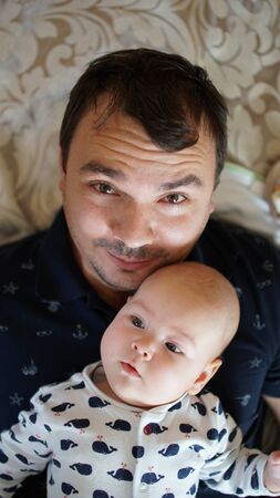 Portrait of loving young man with baby at home . Close up of happy smiling black haired father holding his cute toddler .の写真素材