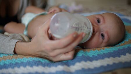 Cute little baby is lying in a bed and sucks milk from a bottle. Feeding baby.