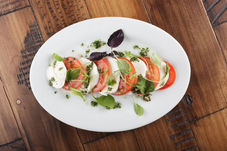 Salad with Mozzarella cheese and tomatoes in white oval plate.の写真素材