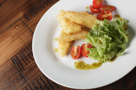 Breaded cheese (deep-fry) with tomatoes and greens in a white plate. Wooden backgroundの写真素材