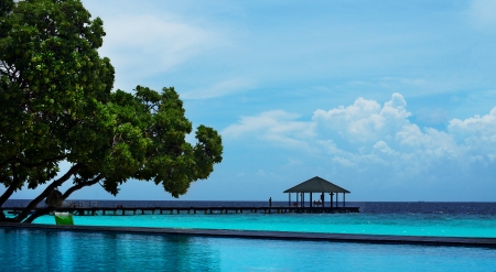 View across a calm blue pool to a pier running out into the sea ending in a a traditional shelter in a beautiful tropical seascapeの写真素材