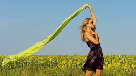 Beautiful woman in a fashionable dress dtanding in front of a field of flowering sunflowers waving a flowing scarf in th breezeの写真素材