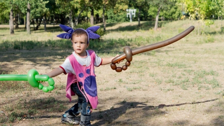 Little boy with a fancy headdress having fun playing in the park with balloon swordsの写真素材