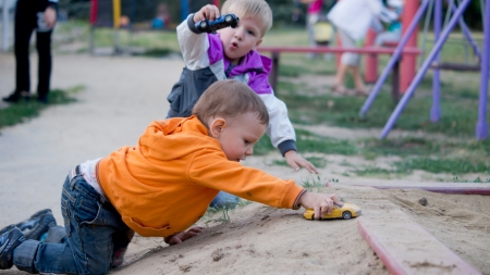 Two little boys crawling on the ground playing with toy cars at a childrens playgroundの写真素材