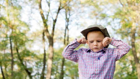 Low angle view of an upset frowning little boy with his hands balled into fists on either side of his forehead outside in woodland with copyspaceの写真素材