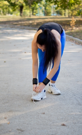 Woman athlete in sportswear bending down and tying her shoelaces on her trainers before starting her exercises in the parkの写真素材