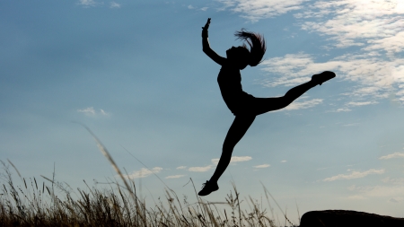 Silhouette of a graceful gymnast or acrobat with a shapely figure leaping high against a blue...