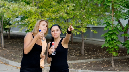 Woman athlete pointing her hand and showing something to her teammate as they stop during training for a drink of waterの写真素材