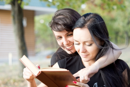 Two young women in a close embrace laughing together at the contents of a bookの写真素材