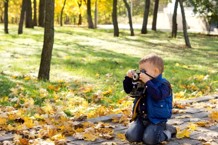 Small boy using a vintage slr camera kneeling on the ground looking through the viewfinder as he composes his shotの写真素材