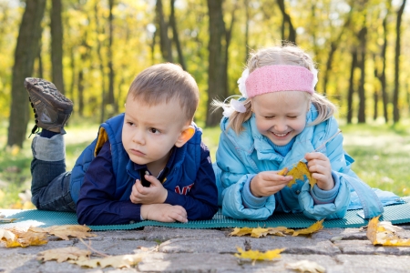 Young brother and sister relaxing and playing with fallen leaves in an autumn woodlandの写真素材