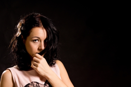 Shy bashful young woman pulling her hair across her face , head and shoulders portrait in darkness with copyspaceの写真素材