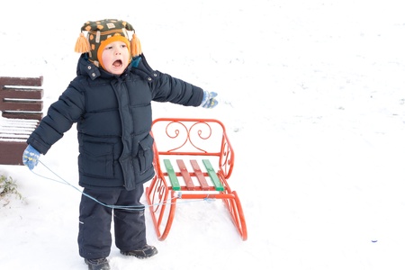 Small boy playing with a sled or toboggan in snow laughing as he enjoys himself pulling it along