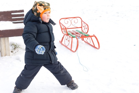 Little boy playing in winter snow standing with his legs straddled looking into the distance with...