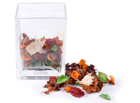 Colorful natural pot pourri with dried seasonal flowers, leaves and spices on a white background alongside a half full glass container for a scented fragrance in the houseの写真素材