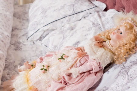 Beautiful vintage doll with curly blonde hair in ringlets and dressed in nineteenth century style lying on a pillowの写真素材