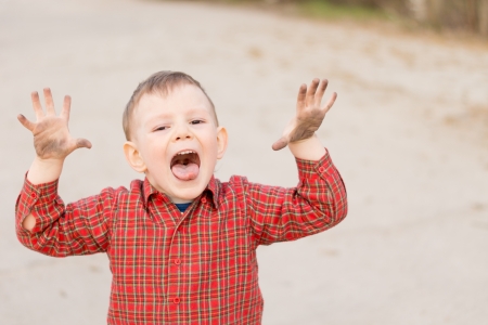 Cute little boy trying to scare the viewer with his hands raised and mouth open yelling, high angle portrait outdoorsの写真素材