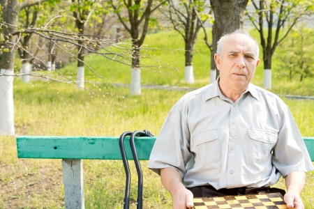 Senior man holding a chessboard and sitting outdoorsの写真素材