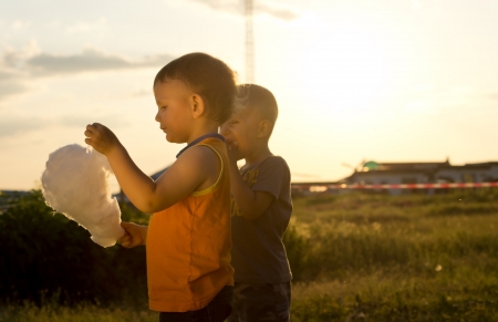 Portrait of two young boys sharing a cotton-candy ball while walking outdoors in the sunsetの写真素材