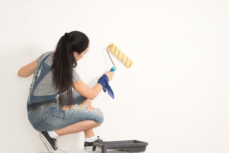 Young woman redecorating her house painting a wall with a rollerの写真素材