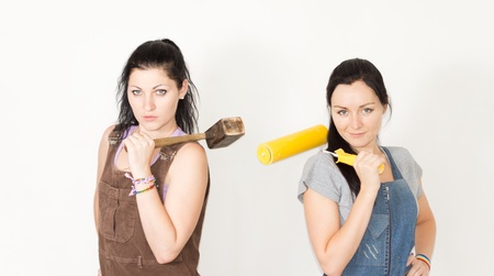 Two attractive young DIY females posing with a wooden mallet and paint roller slung over their shoulders smiling at the cameraの写真素材