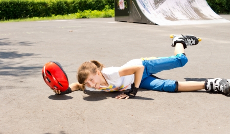 Young girl falling while roller skating lying sprawled on the tarmac with her helmet in her hand and leg in the airの写真素材
