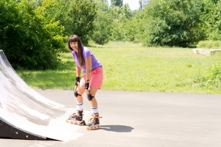 Young girl roller skating poised at the bottom of a cement ramp at a rural skate park smiling at the cameraの写真素材