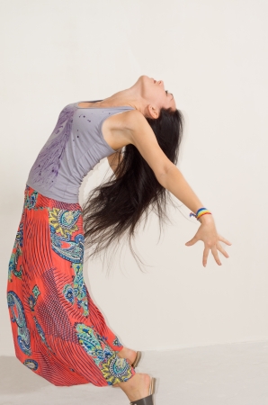 Agile young woman arching her back with her arms outstretched and her long straight brunette hair flying backwardsの写真素材