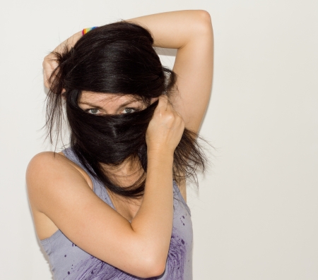 Woman wrapping her long brunette hair around her face so that only her eyes remain visible like an exotic dancer or masked banditの写真素材