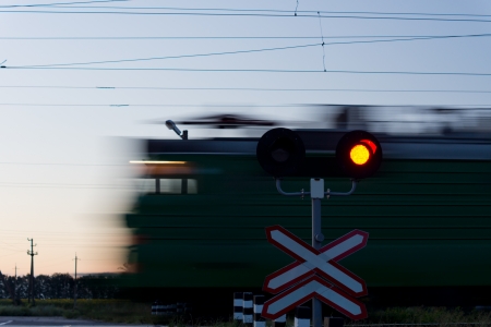 Speeding train passing a level crossing with a red signal in the foreground to prevent cars crossing the lineの写真素材