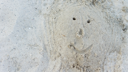 Close-up of an optimistic smiling face traced in wet sandの写真素材