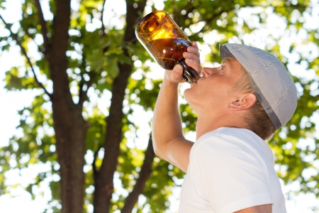 Profile portrait of a middle-aged man drinking from a bottle outdoors with blurred branches and foliage in the backgroundの写真素材