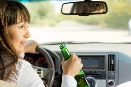 Drunk female driver drinking alcohol from the bottle turning and talking to a passenger while driving down a road losing all concentrationの写真素材