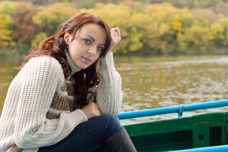 Beautiful young woman out boating sitting in a rowboat on a lake or river in autumn looking pensively at the camera, close up portraitの写真素材